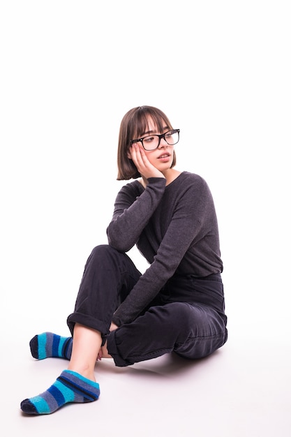 Ragazza adolescente con gli occhiali seduto sul pavimento isolato