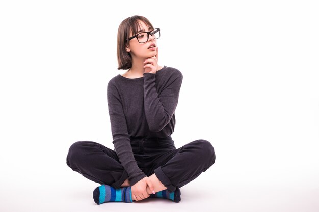 Ragazza adolescente con gli occhiali seduto sul pavimento isolato