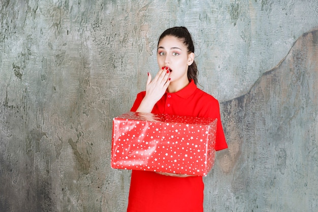 Ragazza adolescente con in mano una scatola regalo rossa con puntini bianchi e sembra spaventata e terrorizzata
