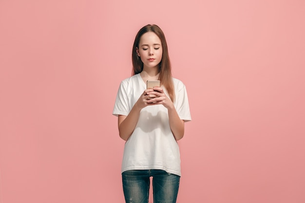 Ragazza adolescente felice in piedi, sorridente con il telefono cellulare su studio rosa alla moda.