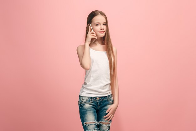 Ragazza adolescente felice in piedi, sorridente con il telefono cellulare su studio rosa alla moda.