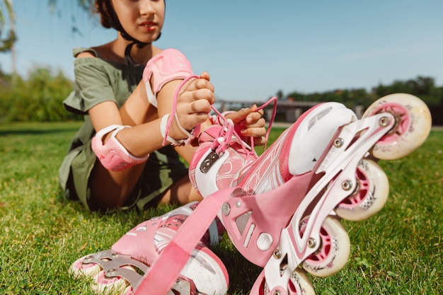 Ragazza adolescente in un casco impara a guidare sui pattini a rotelle tenendo un equilibrio o sui rollerblade e girare per la strada della città nella soleggiata giornata estiva