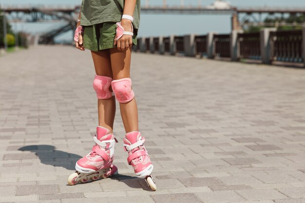 Ragazza adolescente in un casco impara a guidare sui pattini a rotelle tenendo un equilibrio o sui rollerblade e girare per la strada della città nella soleggiata giornata estiva