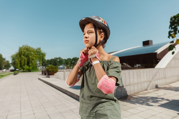 Ragazza adolescente in un casco impara a guidare sui pattini a rotelle tenendo un equilibrio o sui rollerblade e girare per la strada della città nella soleggiata giornata estiva