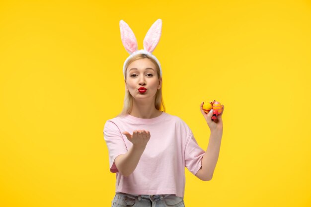 Ragazza adorabile bionda adorabile di Pasqua con le orecchie rosa del coniglietto e il rossetto rosso che inviano i baci