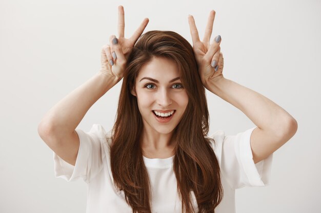 Ragazza adorabile sciocca che mostra il gesto del coniglietto e sorridere felice