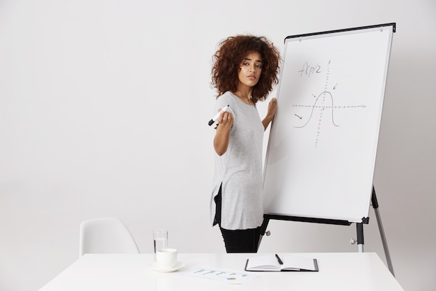 Ragazza africana che sta lavagna vicina dell'indicatore nel luogo di lavoro.