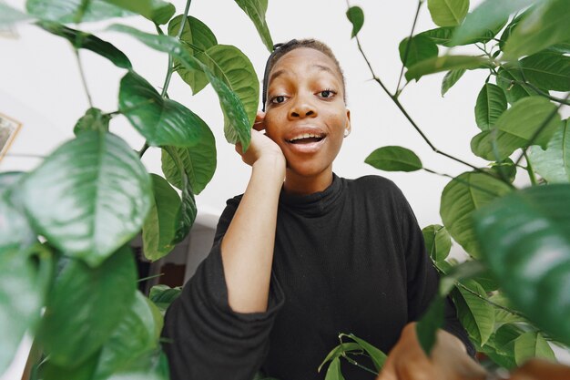 Ragazza africana in una stanza. Ragazza alla moda vicino alla pianta. Signora in un maglione nero.