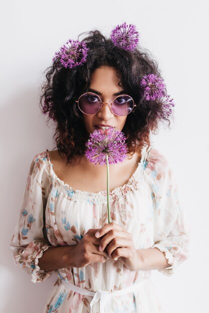 Ragazza africana riccia felice che tiene allium viola. donna castana alla moda in posa con i fiori.