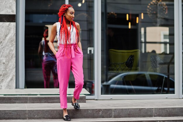 Ragazza afroamericana alla moda con pantaloni rosa e dreadlocks rossi poste all'aperto