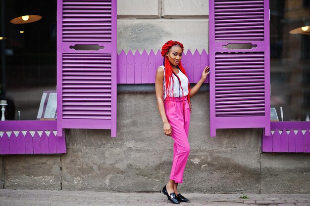 Ragazza afroamericana alla moda con pantaloni rosa e dreadlocks rossi poste all'aperto