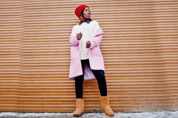 Ragazza afroamericana con cappello rosso e cappotto rosa contro persiane arancioni