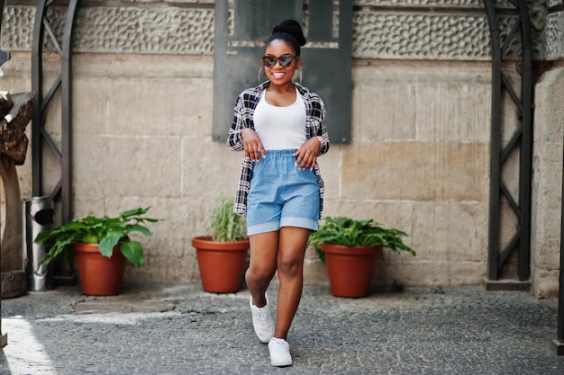 Ragazza afroamericana hip hop su occhiali da sole e pantaloncini di jeans Ritratto di moda di strada casual di donna nera