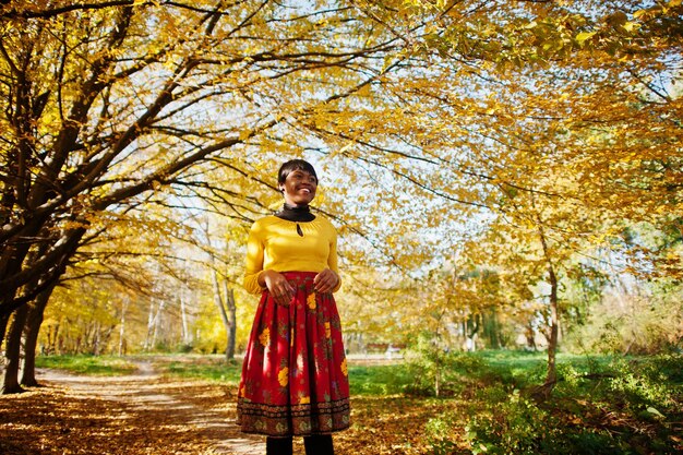 Ragazza afroamericana in abito giallo e rosso al parco autunnale dorato