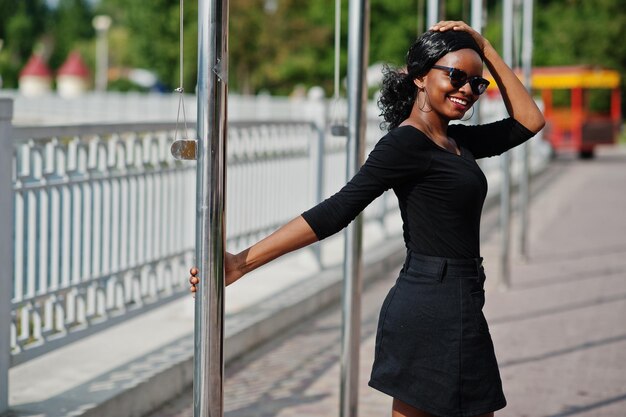 Ragazza afroamericana in occhiali da sole vestiti neri e camicia poste all'aperto Donna nera alla moda