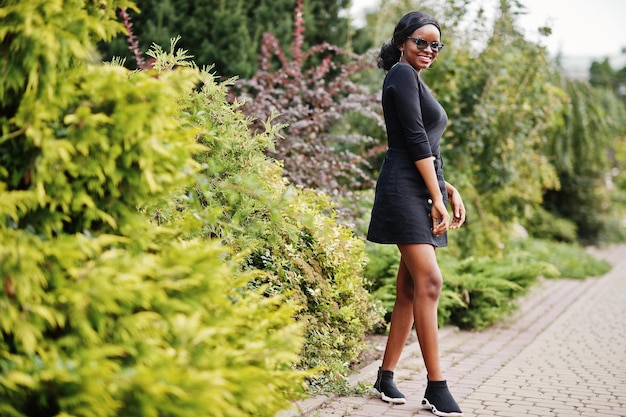 Ragazza afroamericana in occhiali da sole vestiti neri e camicia poste all'aperto Donna nera alla moda