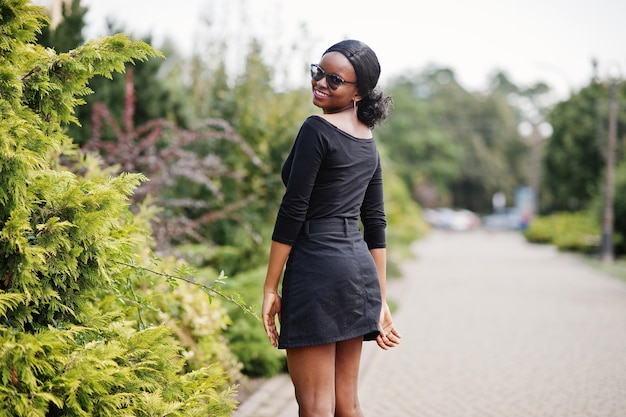 Ragazza afroamericana in occhiali da sole vestiti neri e camicia poste all'aperto Donna nera alla moda