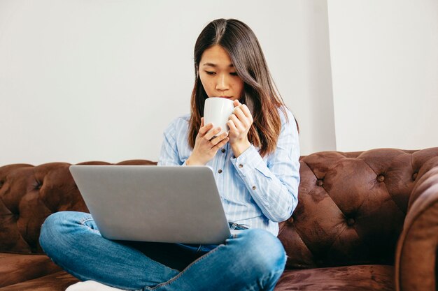 Ragazza agghiacciante che mangia caffè e che guarda computer portatile