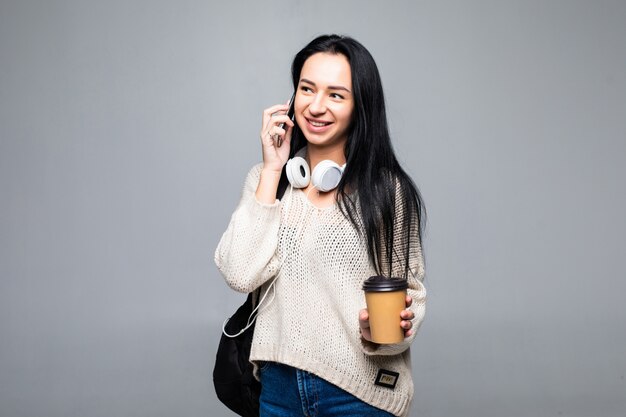 Ragazza alla moda attraente che ride allegramente mentre parla sul telefono cellulare con il suo ragazzo, isolato sulla parete grigia. Concetto di conversazione.