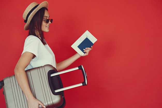 Ragazza alla moda che posa con l'attrezzatura di viaggio su una parete rossa