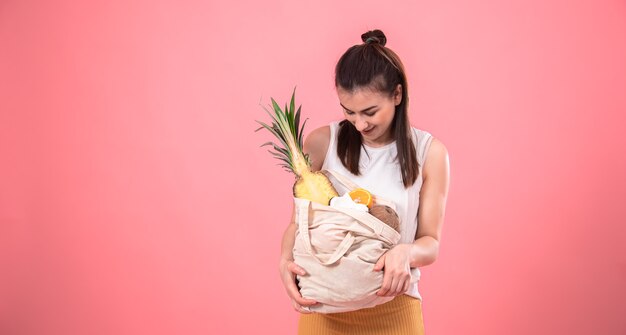 Ragazza alla moda che sorride e che tiene una borsa ecologica con frutti esotici