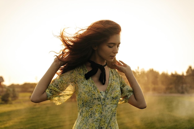 Ragazza alla moda con le lentiggini da acconciatura volpe e la benda nera sul collo in un moderno vestito giallo in posa e guardando in basso all'aperto