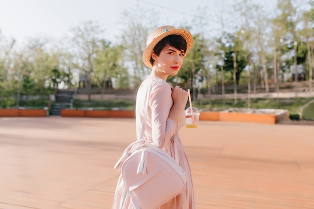 Ragazza alla moda con taglio di capelli corto guarda con interesse sopra la sua spalla durante la passeggiata nel parco