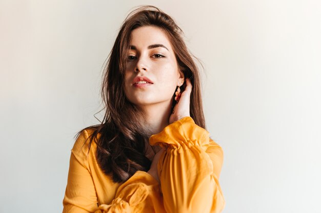 Ragazza alla moda senza trucco in posa sul muro bianco. Ritratto di donna in camicetta gialla.