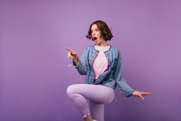 Ragazza alla moda sorpresa con i capelli castani che salta. incantevole donna in pantaloni attillati.