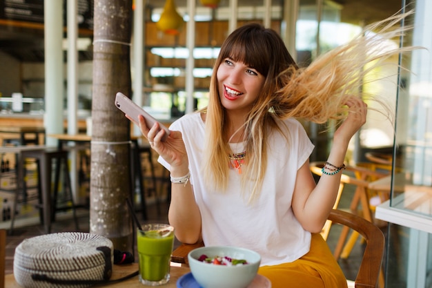 Ragazza allegra che gode della prima colazione saporita durante le vacanze in caffè moderno alla moda.