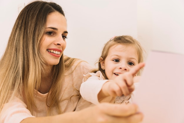 Ragazza allegra che indica libro mentre leggendo con la madre