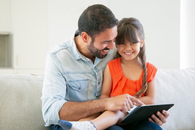 Ragazza allegra che si siede sulle ginocchia di suo padre, che guarda l'obbiettivo e ridendo.