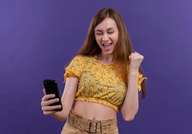 Ragazza allegra che tiene il telefono cellulare e solleva il pugno sullo spazio viola isolato