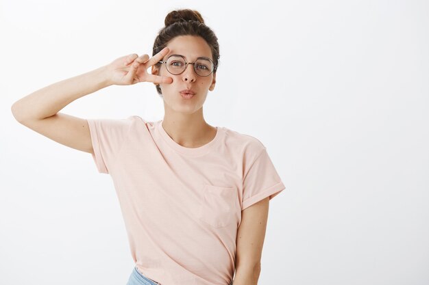 Ragazza allegra con gli occhiali in posa contro il muro bianco