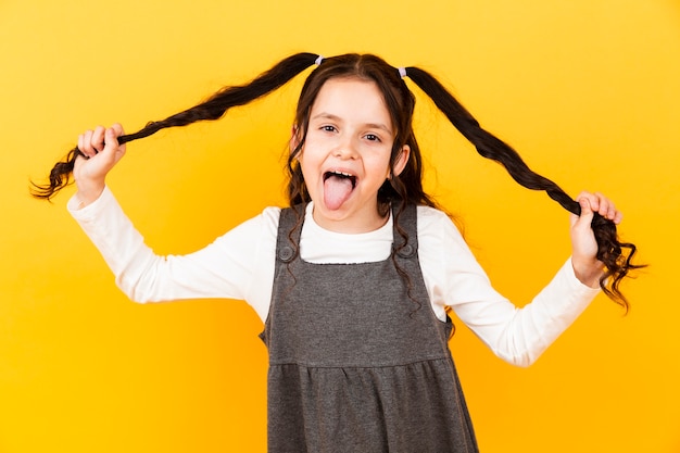 Ragazza allegra con la lingua fuori mentre si tiene i capelli trecce