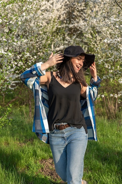 Ragazza allegra con un cappello tra gli alberi in fiore in primavera, in uno stile casual