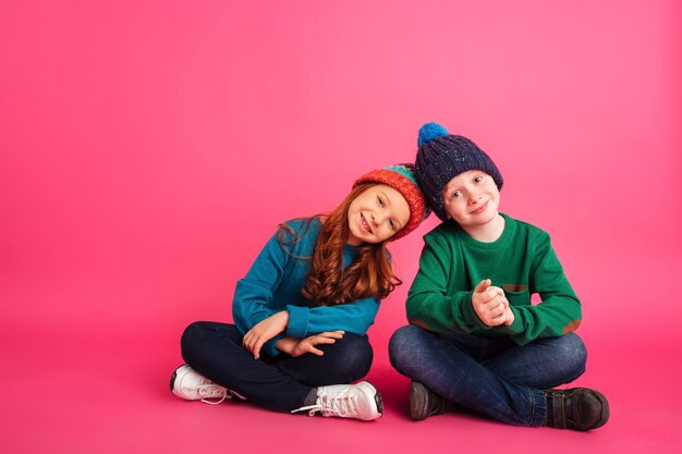 Ragazza allegra e suo fratello che si siedono sul pavimento e che sorridono alla macchina fotografica