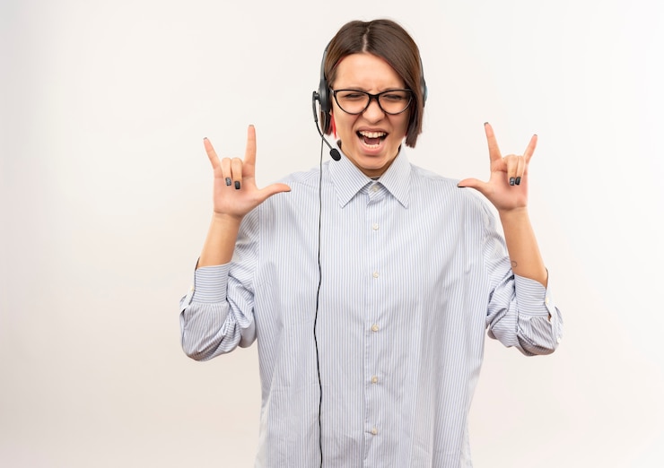 Foto gratuito ragazza allegra giovane call center con gli occhiali e auricolare facendo segni di roccia con gli occhi chiusi isolati su bianco