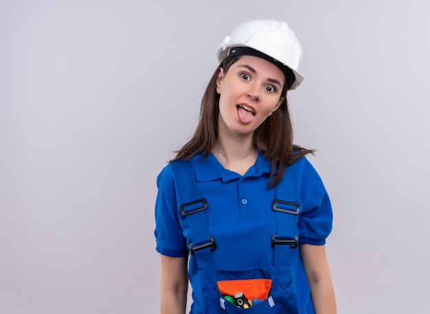 Ragazza allegra giovane costruttore con casco di sicurezza bianco e uniforme blu guarda la telecamera su sfondo bianco isolato con spazio di copia