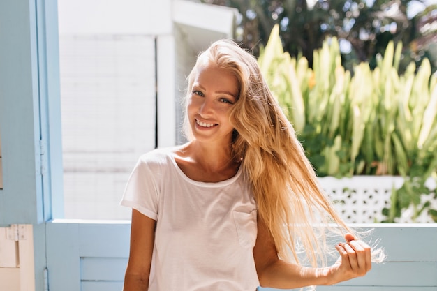 Ragazza allegra leggermente abbronzata con un sorriso sincero in posa. graziosa donna caucasica tenendo i suoi capelli biondi.