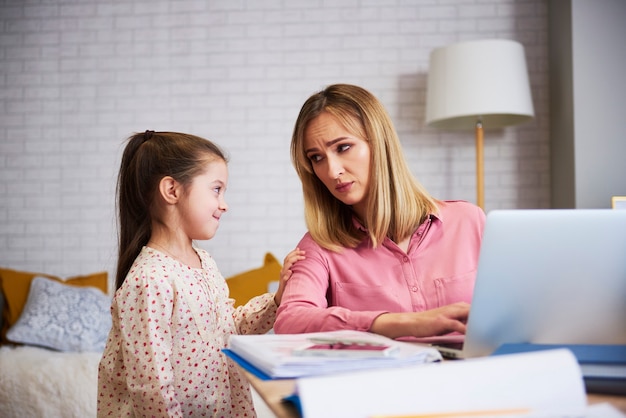 Ragazza annoiata con una giovane mamma che lavora sodo a casa in ufficio