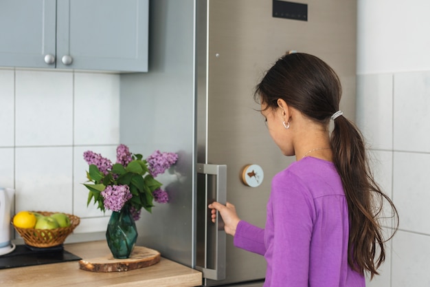 Ragazza aprendo il frigo in cucina