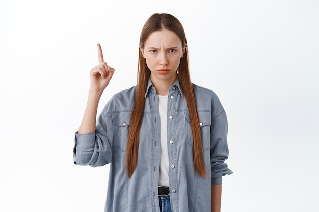 Ragazza arrabbiata e imbronciata che si acciglia, indica una cosa ingiusta, è gelosa o turbata, si lamenta, rimane delusa su sfondo bianco.