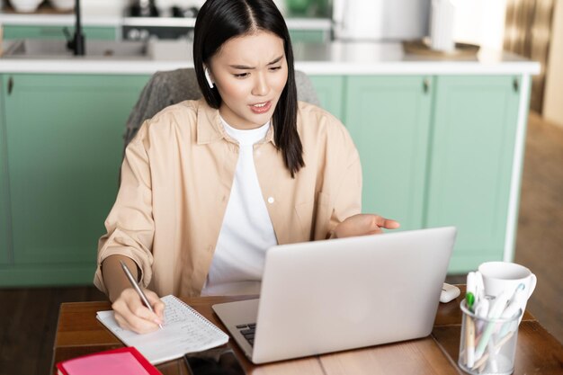 Ragazza asiatica che lavora in videoconferenza sul laptop da casa parlando in video chat con la faccia interessata