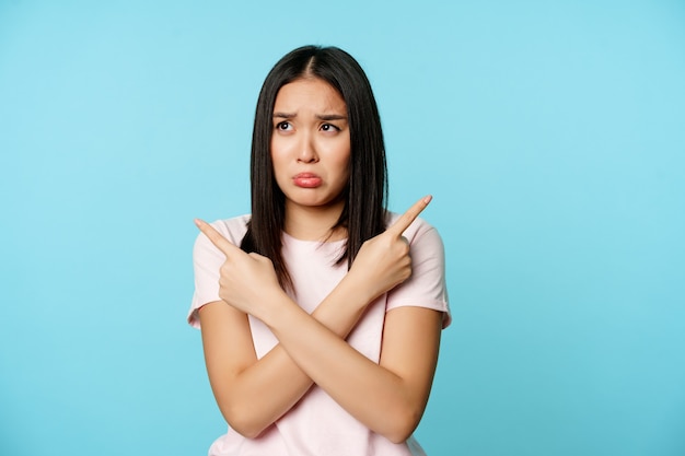 Ragazza asiatica confusa e triste che punta lateralmente cercando problemi all'oscuro o indecisi con la scelta di p...