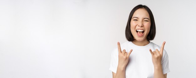 Ragazza asiatica impertinente che grida godendosi un concerto o un festival che mostra il rock sul cartello di metalli pesanti divertendosi s