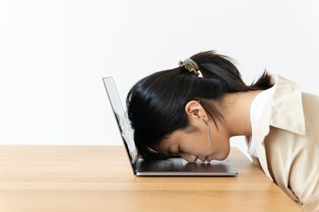 Ragazza asiatica sollecitata che riposa la sua testa su un computer portatile