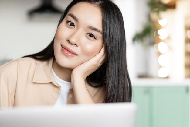 Ragazza asiatica sorridente che si siede con il computer portatile che lavora al pc del computer