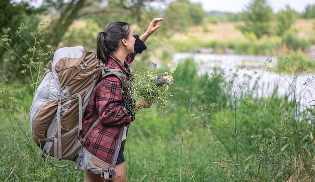 Ragazza attraente con un grande zaino da viaggio e un mazzo di fiori di campo.