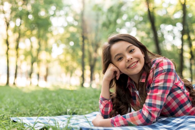 Ragazza attraente felice che esamina macchina fotografica che si trova nel parco